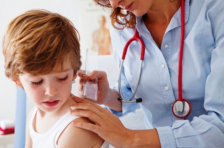 O médico examina a un neno con papiloma no corpo